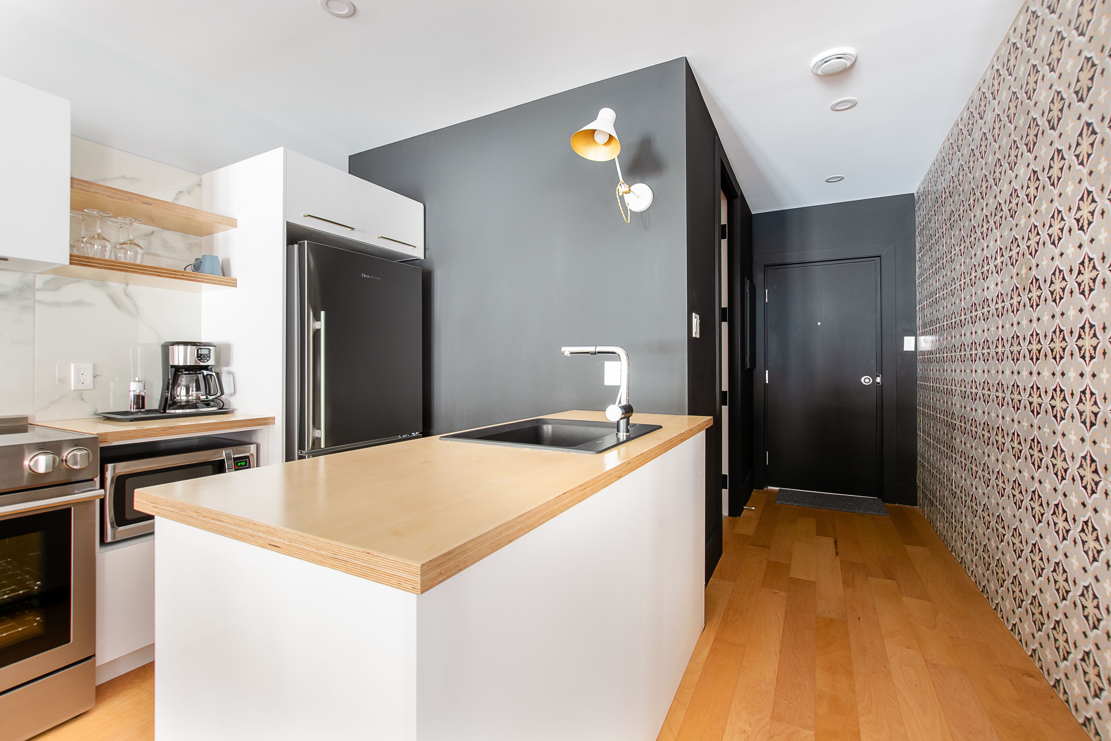 A modern kitchen with a central island, stainless steel appliances, and a patterned wall.