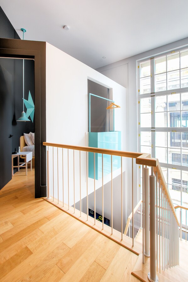 Un interior moderno con una escalera de madera, vistas de la ciudad a través de amplias ventanas y una lámpara con diseño geométrico.