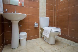 Un baño con lavamanos, inodoro y cubo de basura blancos.