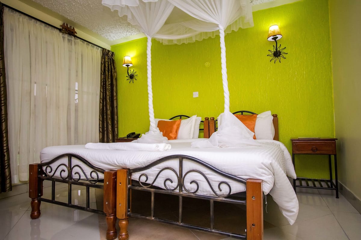 Cama bem arrumada com lençóis brancos, cabeceira de madeira e mesa de cabeceira com abajur.