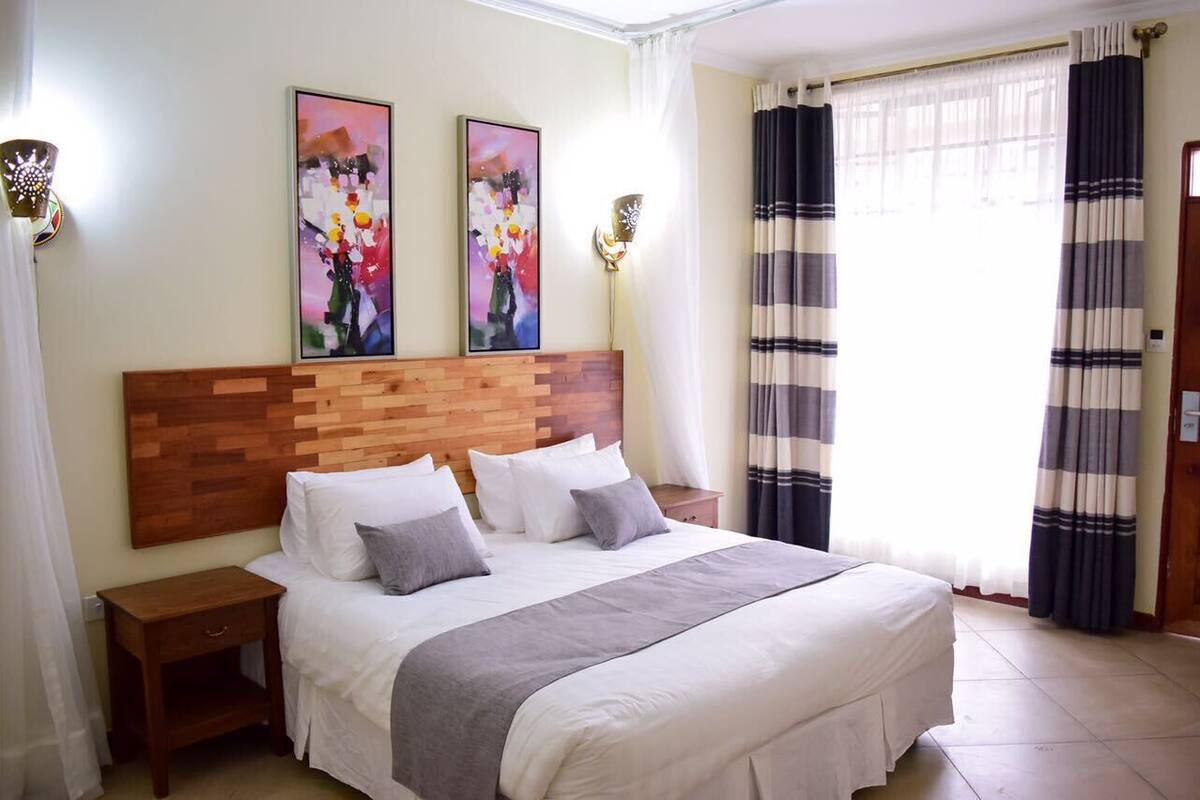 Uma cama bem arrumada com cabeceira de madeira, duas luminárias fixadas na parede e dois quadros na parede.