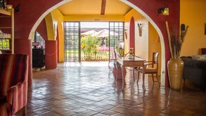Una habitación amplia con suelo de baldosas, una mesa de madera con sillas, un sofá y un jarrón grande.