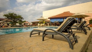 Un área junto a la piscina con sillones de descanso, sombrillas y suelo de baldosas.