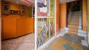Un espace d’accueil doté d’un comptoir en bois, d’un mur en verre orné de peintures d’animaux et d’un escalier aux marches orange.