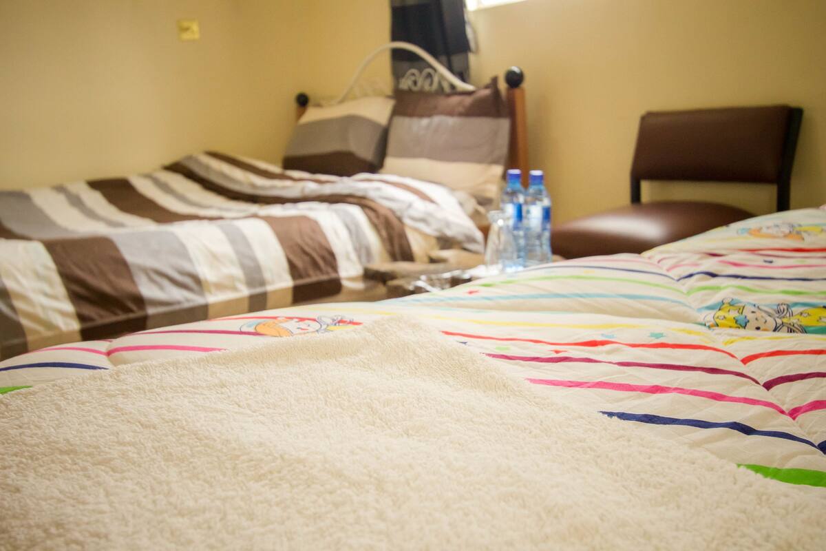 A hotel room with two beds, a chair, and a table with water bottles.