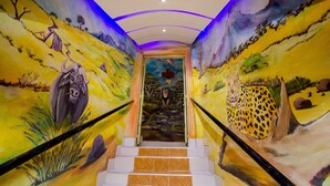 Un escalier orné de fresques colorées représentant la faune et la flore, de part et d’autre, qui mène à une pièce offrant une vue sur le ciel.