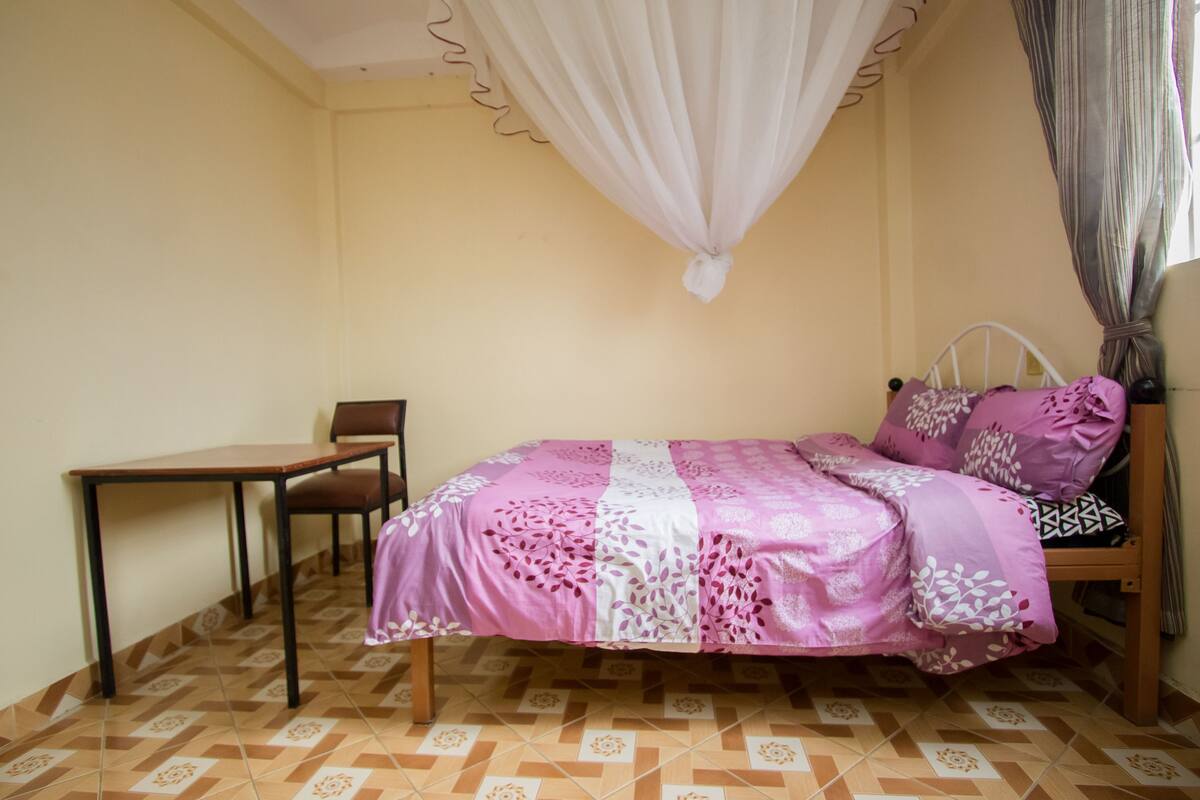 A bedroom with a bed, a chair, a table, and a window with curtains.