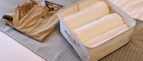 A neatly folded beige shirt and a rectangular, light-colored, padded box on a striped fabric surface.