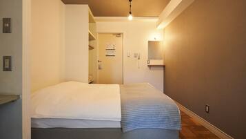 A bedroom with a bed, a bedside table, a nightstand, a wall-mounted light, and a door leading to another room.