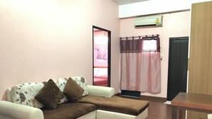 A living room with a sofa, a small table, and a curtain. - Ponlaan Apartment (Nakhon Ratchasima)