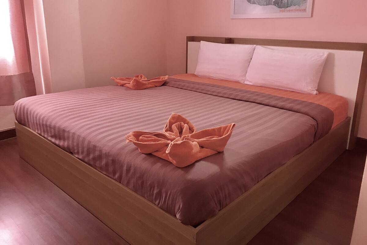 A neatly made bed with a brown and pink striped bedspread, two pillows, and a decorative towel arrangement.