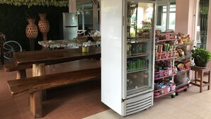 A food kiosk with a Haier refrigerator, a wooden bench, and a shelf with snacks and drinks. - Ponlaan Apartment (Nakhon Ratchasima)