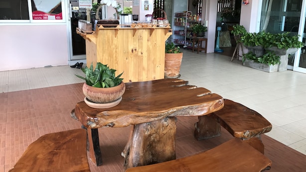 A wooden bench with a rustic design, a potted plant, and a wooden counter with various items. - Ponlaan Apartment (Nakhon Ratchasima)