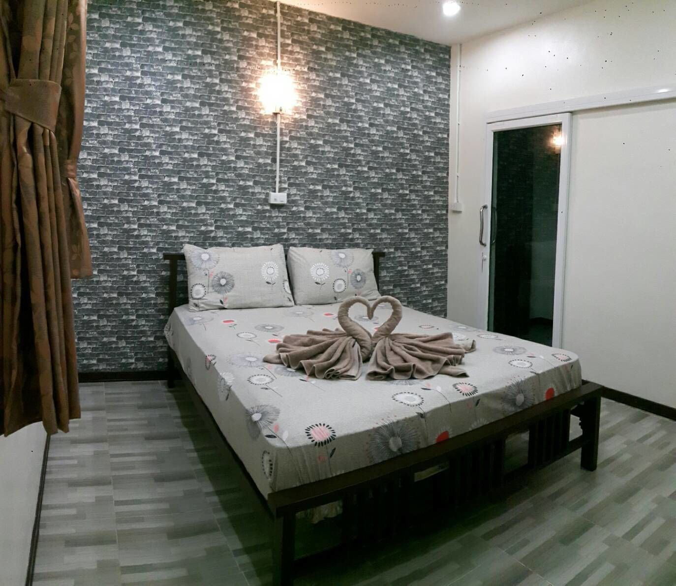 A bedroom with a brick-patterned wall, a bed with a heart-shaped towel arrangement, and a sliding door.