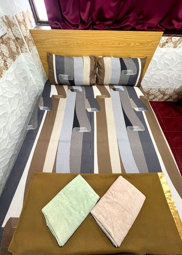 Un lit bien fait, avec une literie à rayures, une tête de lit en bois et deux oreillers. Deux serviettes pliées sont posées sur un plateau marron.