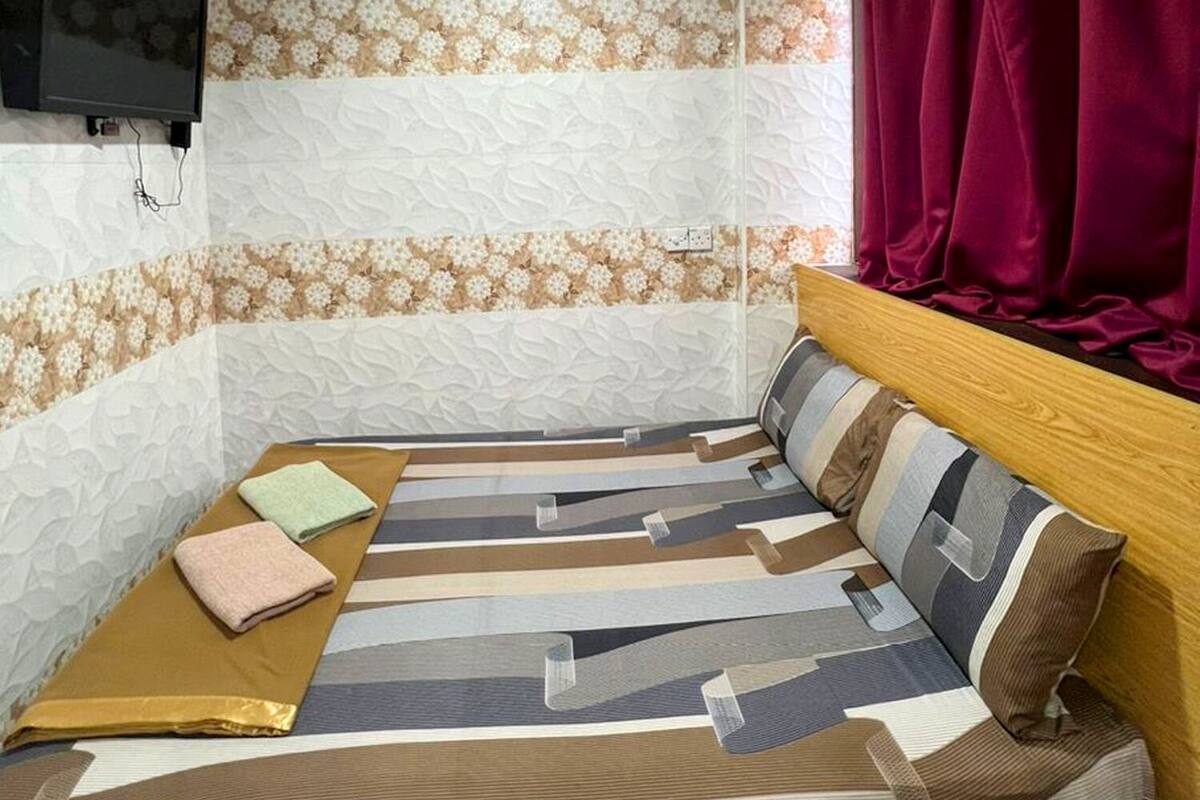 Una stanza con un letto, una televisione a parete e una finestra con tende.