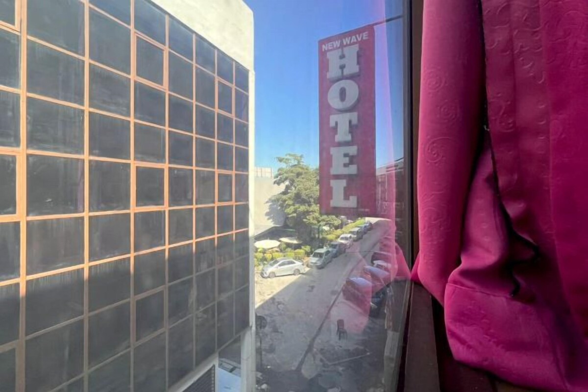 Een uitzicht op een gebouw met een grote glazen gevel en een bord met daarop 'NEW WAVE HOTEL' aan de rechterkant.