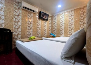 Une chambre d’hôtel avec deux lits, un téléviseur fixé au mur et une petite table avec des serviettes.