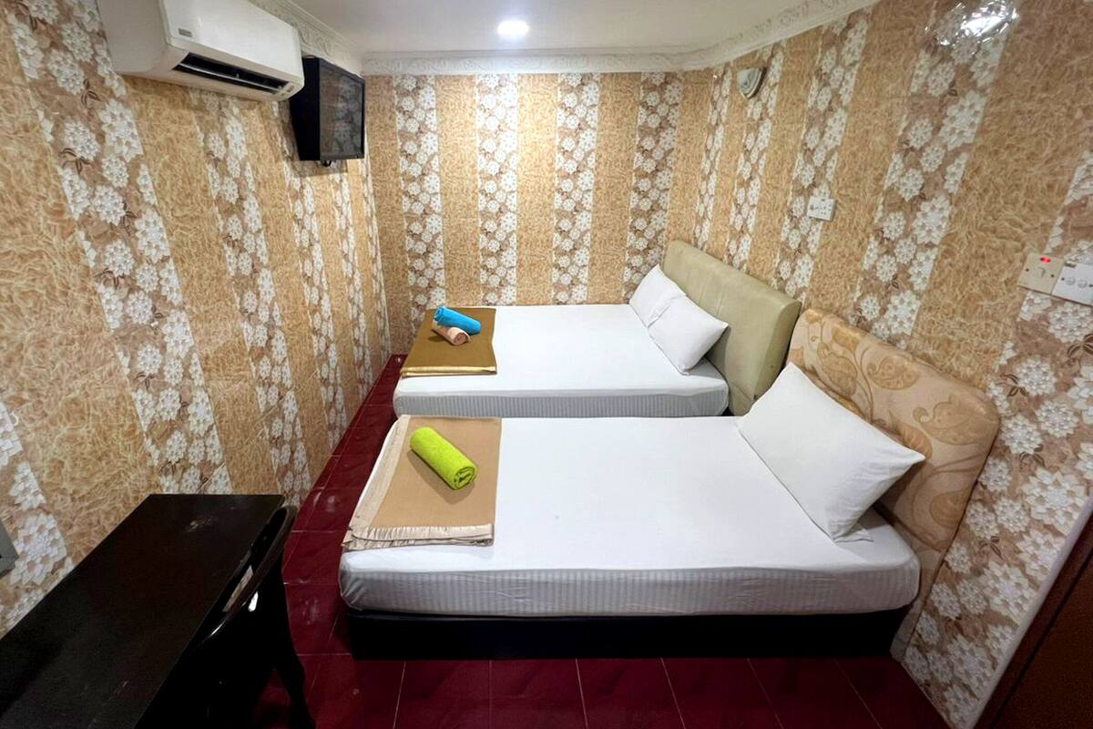 Una camera d'albergo con due letti, una TV e un pavimento piastrellato rosso.
