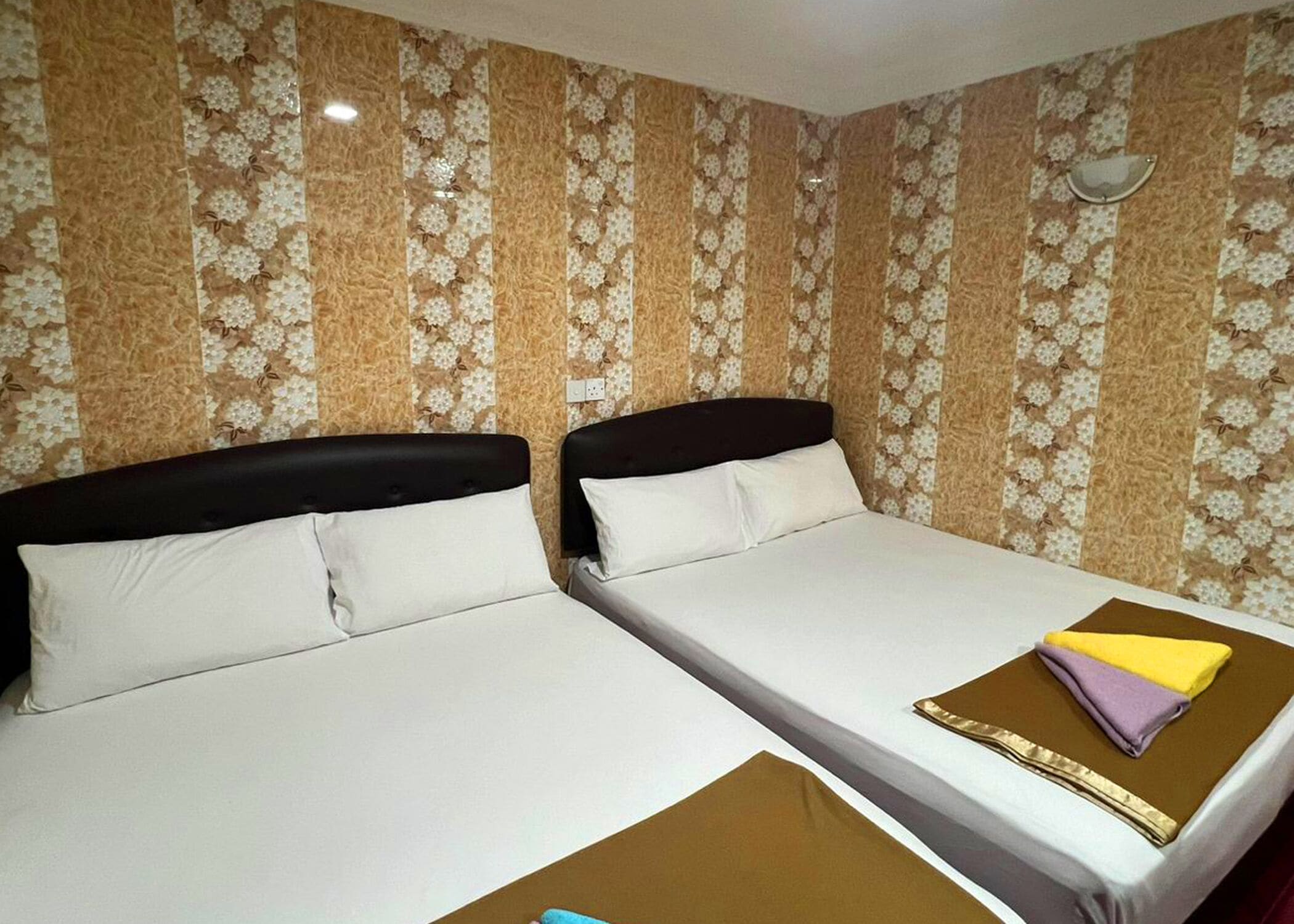A hotel room with two beds, each with a black headboard and white bedding. The walls have a floral patterned wallpaper.