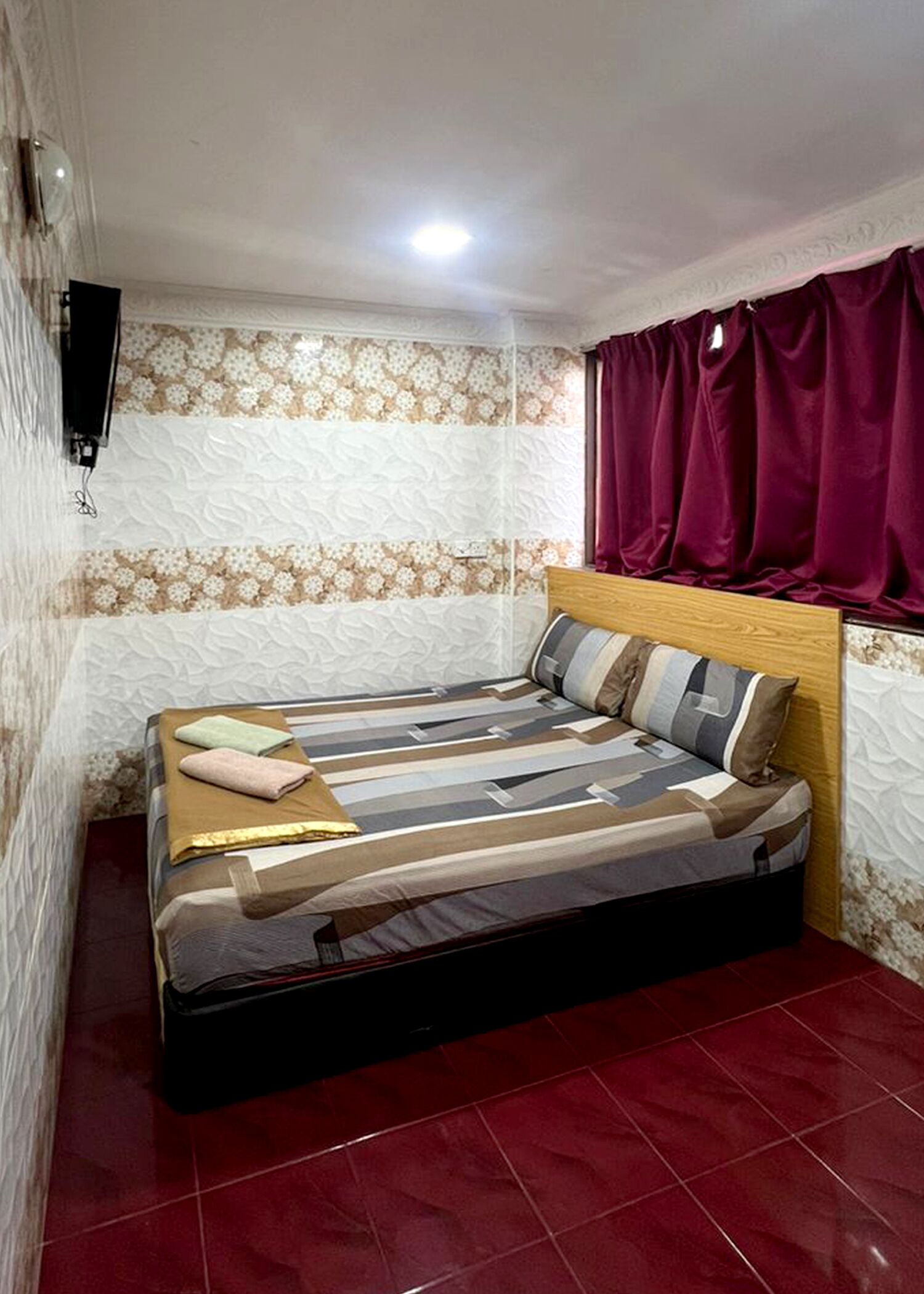 Un dormitorio con una cama, un televisor en la pared y una ventana con cortinas.