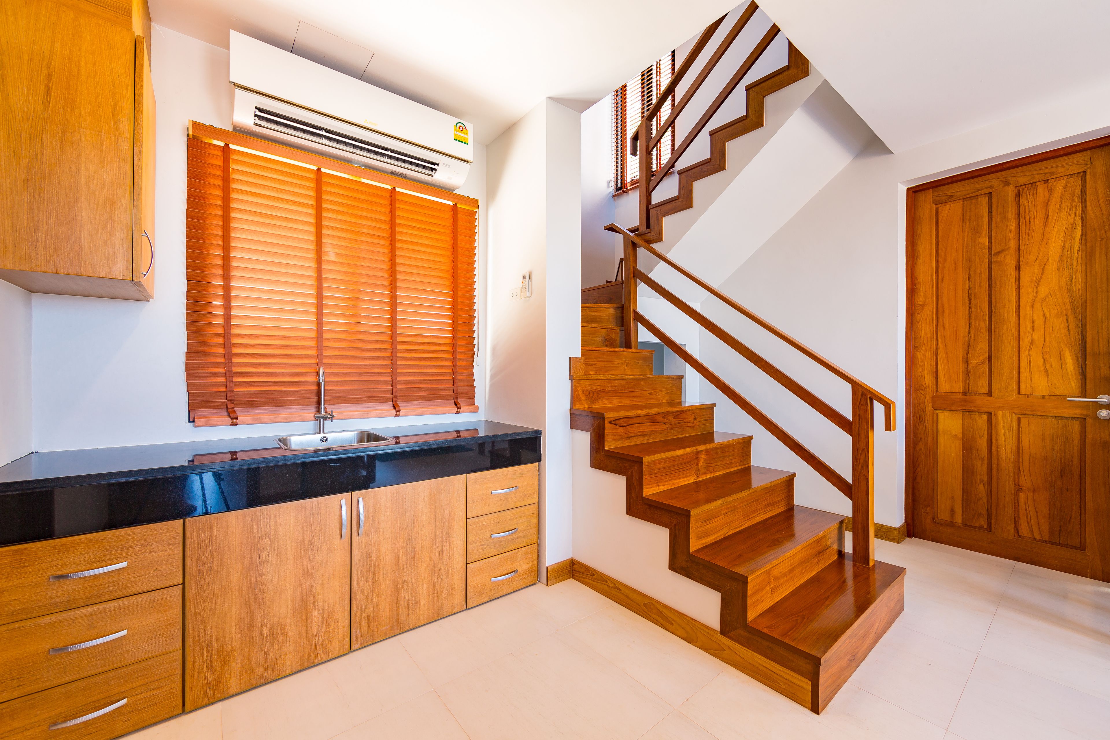 A kitchen with wooden cabinets, a black countertop, and a wooden staircase.