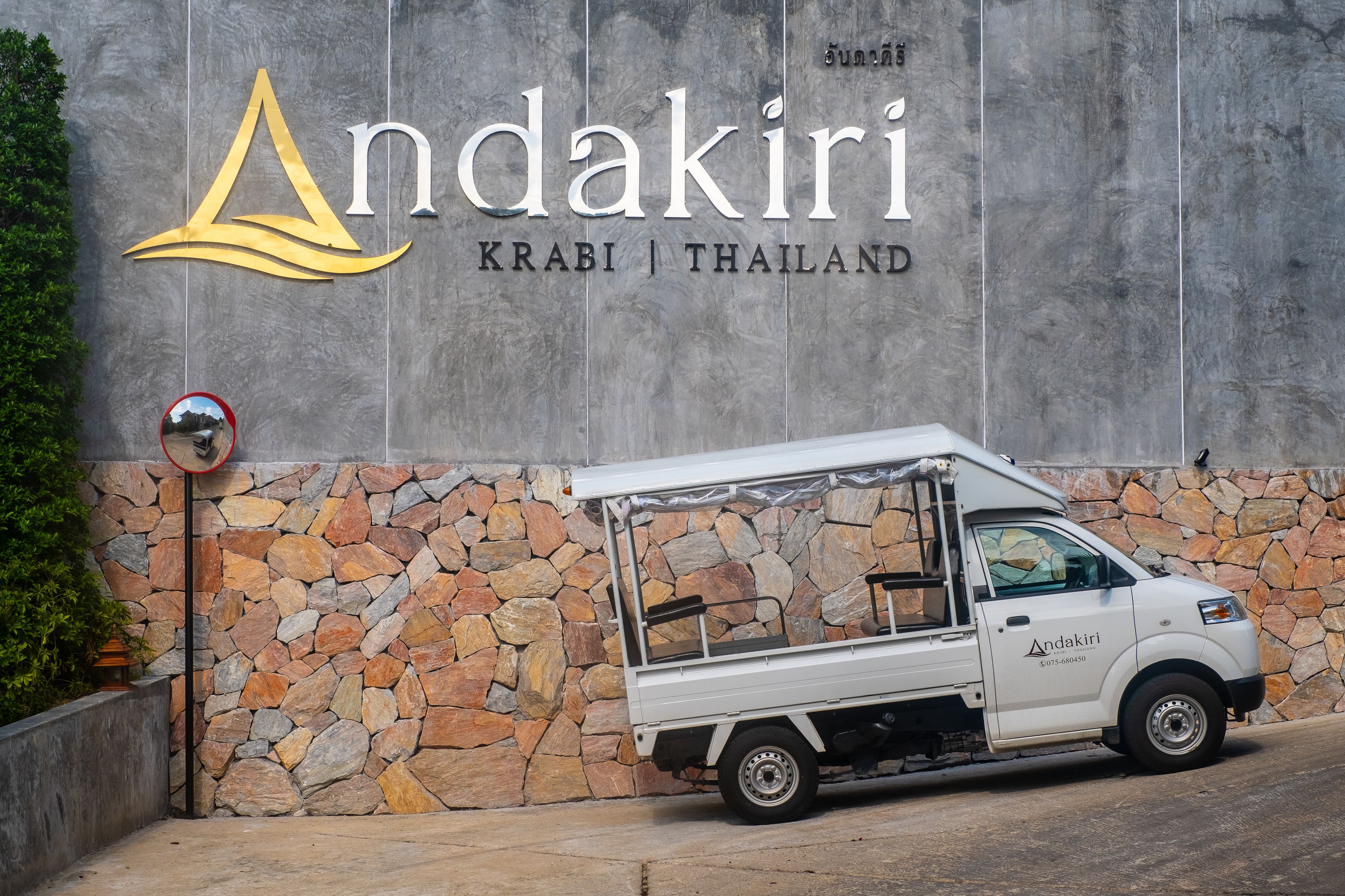 A white truck parked in front of a building with a stone wall and a sign that reads "Andakiri Krabi | Thailand".