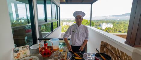 A chef preparing food on a balcony with a city view, buffet setup with various dishes, and a sign indicating an egg station.