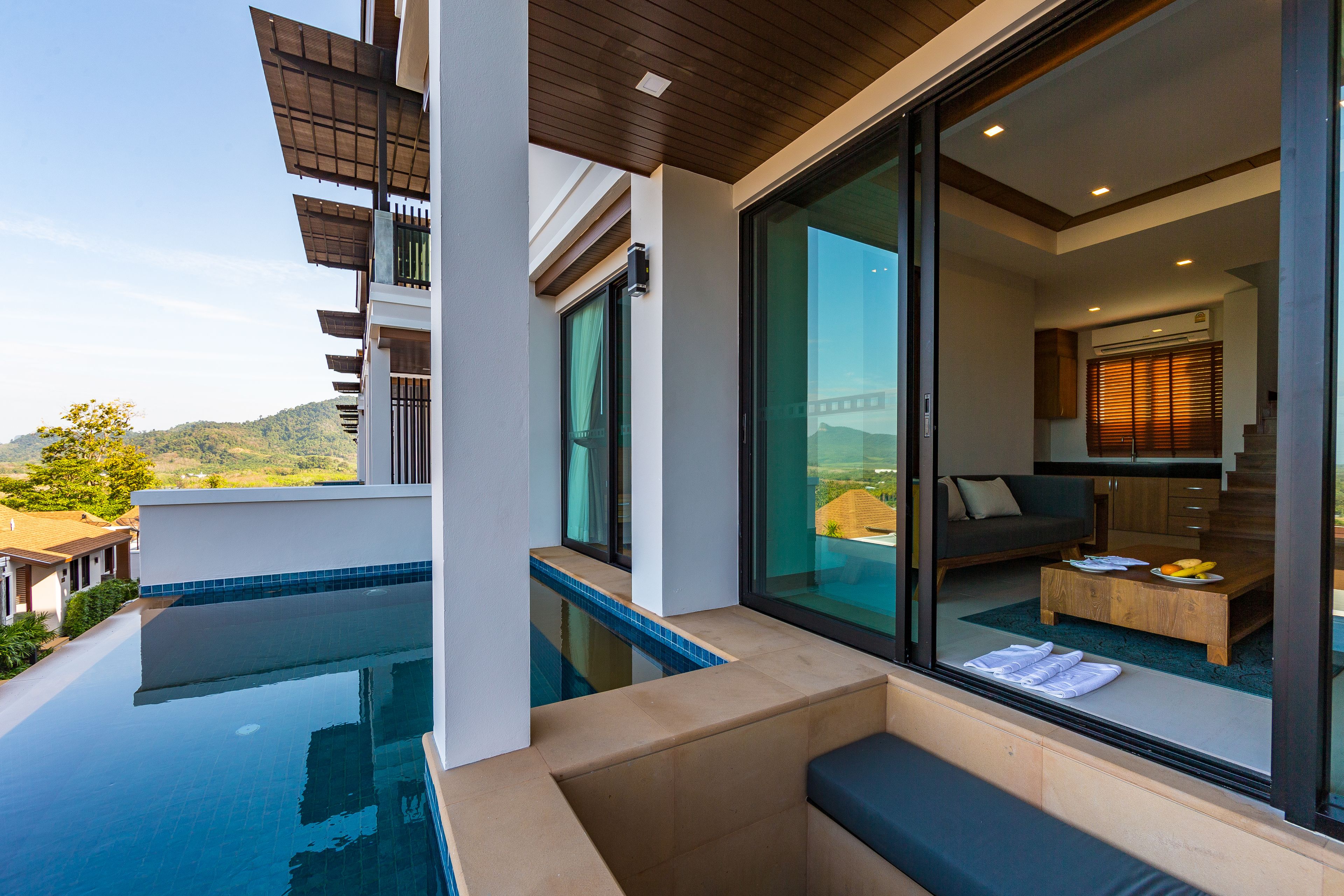 Un área de piscina moderna al aire libre con cerramiento de vidrio, zona de estar y vistas al paisaje.
