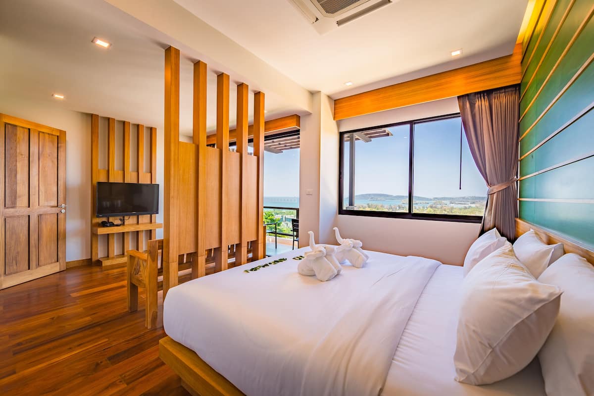 Quarto de hotel moderno com uma cama grande, móveis de madeira, televisão e varanda com vista.