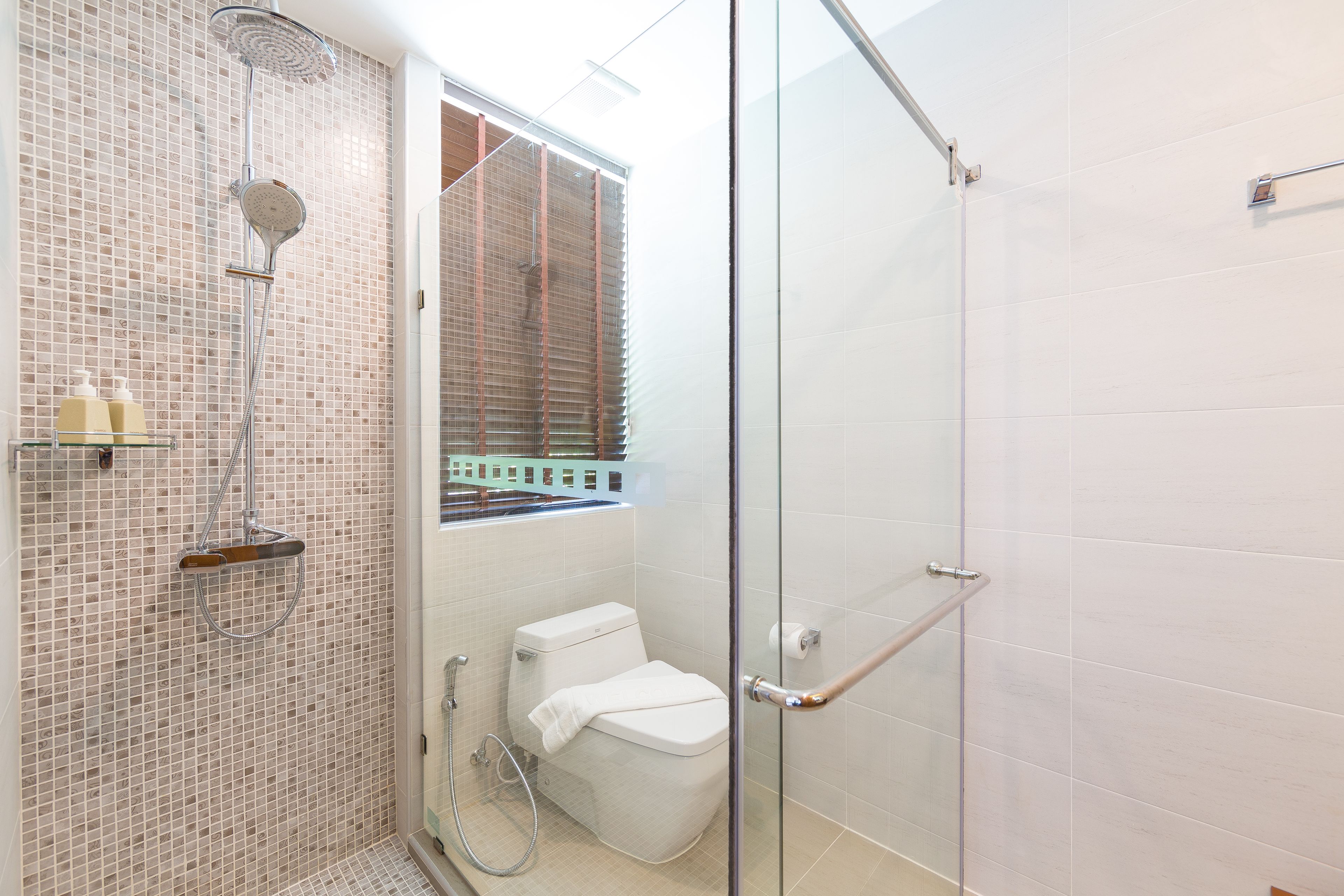 Een moderne badkamer met een douchecabine van glas, een toilet en een klein raam met zonwering.