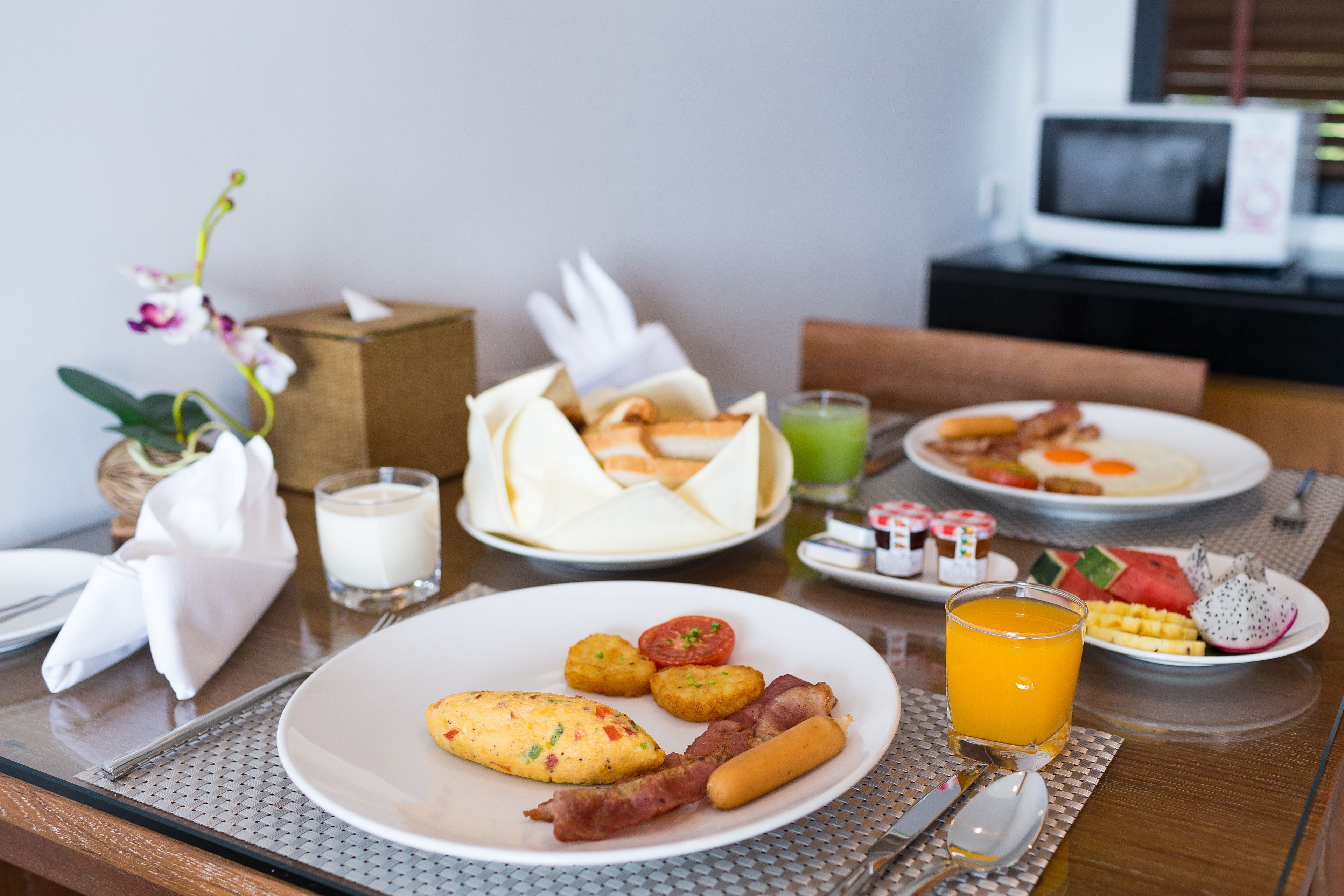 A breakfast table with plates of food, a glass of orange juice, and a microwave in the background.