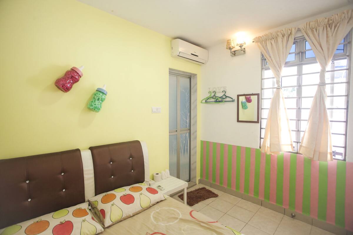 A room with a bed, a window with curtains, a wall-mounted air conditioner, and a small table with a bottle and a cup.