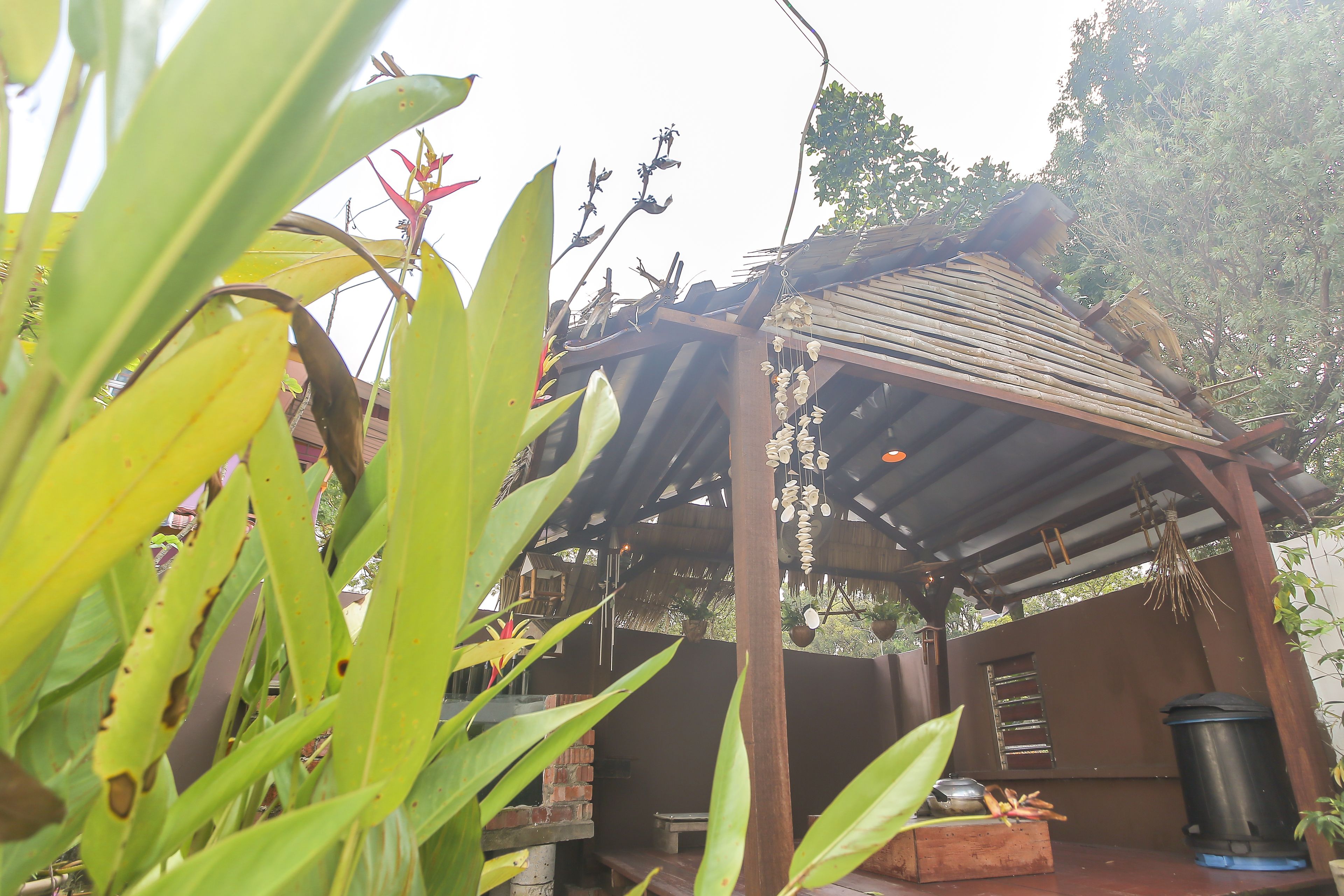 A wooden pergola with hanging decorations, a brick wall, and a trash bin.