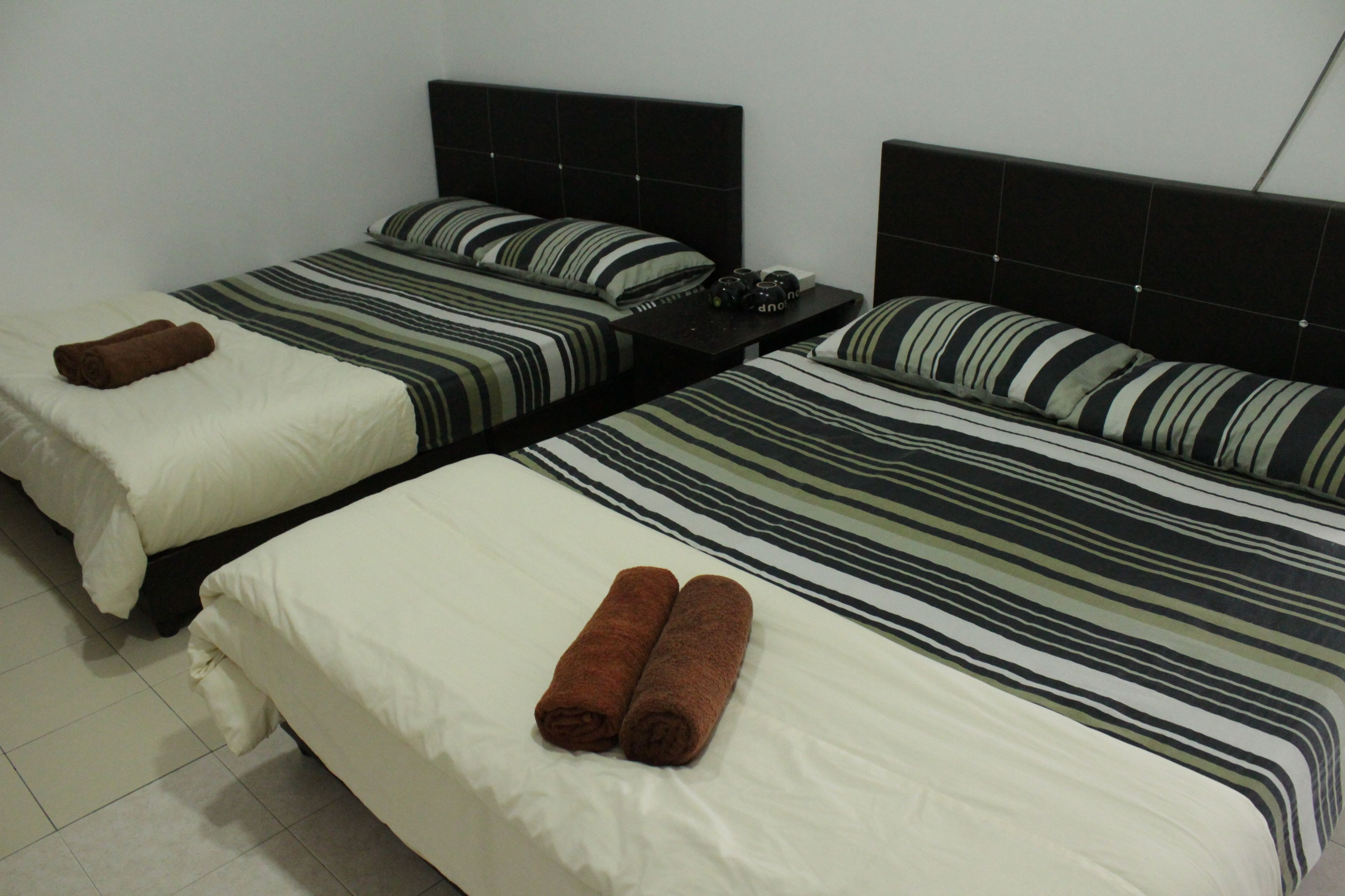 Two single beds with striped bedding and brown towels, a nightstand with a phone and a cup, and a tiled floor.