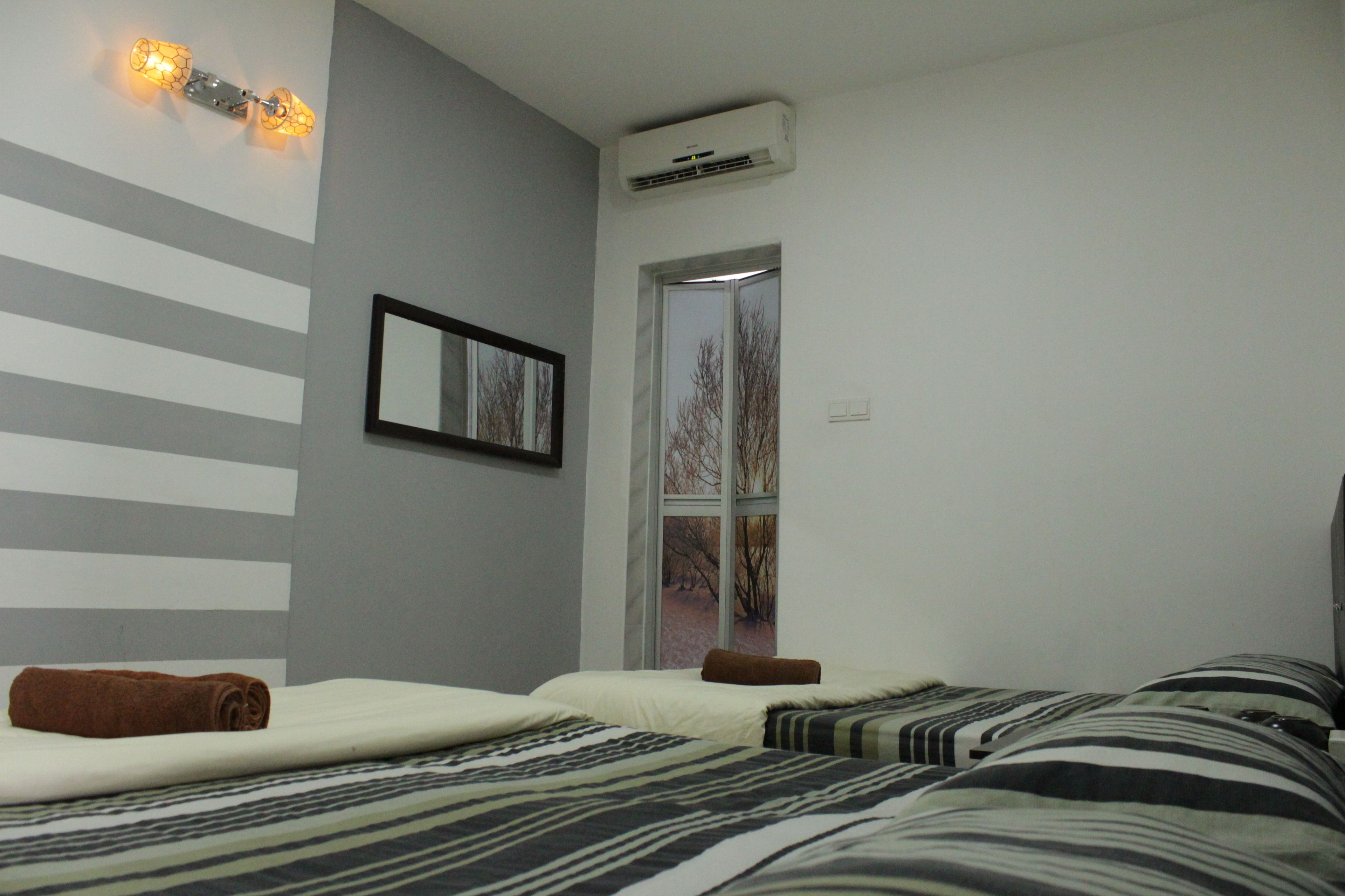 A hotel room with two beds, a window with a view of trees, a wall-mounted air conditioner, and a framed picture.