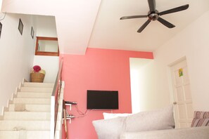 Un escalier menant à une pièce dotée d’un ventilateur de plafond, d’un téléviseur fixé au mur et d’une porte ornée de motifs colorés.