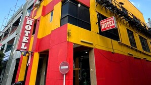 A hotel with a red and yellow facade, a visible entrance, and a sign indicating it is a new hotel.