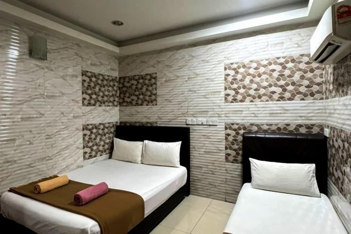Ein Hotelzimmer mit zwei Betten, einer braunen und einer weißen Tagesdecke sowie Wandfliesen mit Muster.