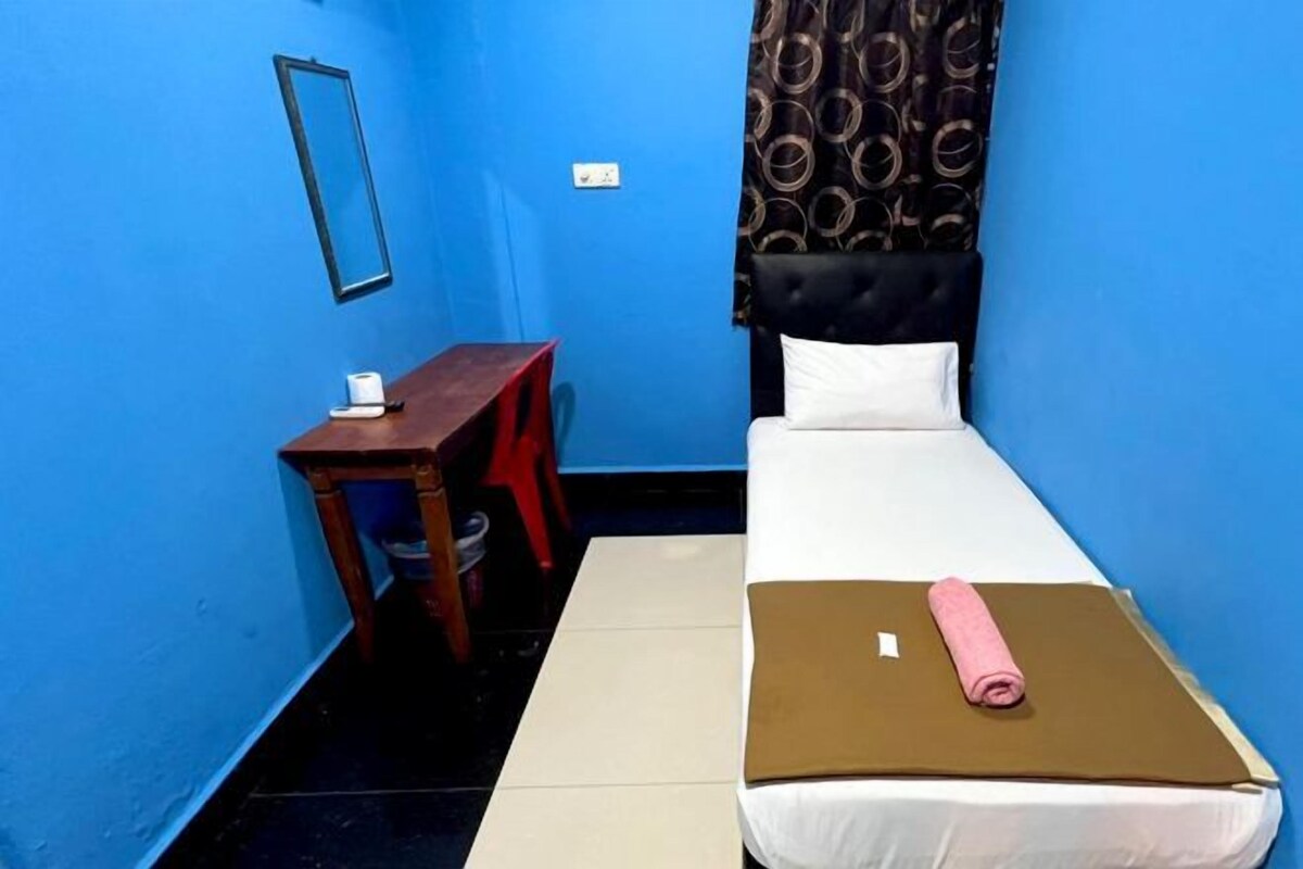 Une petite chambre avec un lit simple, un mur bleu, une table de chevet en bois, une couvre-lit blanche et une couverture marron.