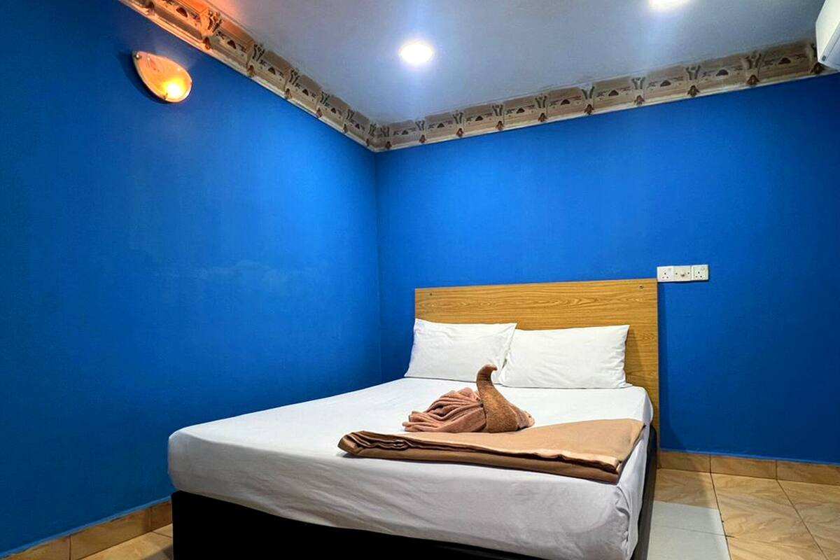 Ein Schlafzimmer mit blauer Wand, einem hölzernen Kopfteil, weißer Bettwäsche und einer braunen Decke auf dem Bett.