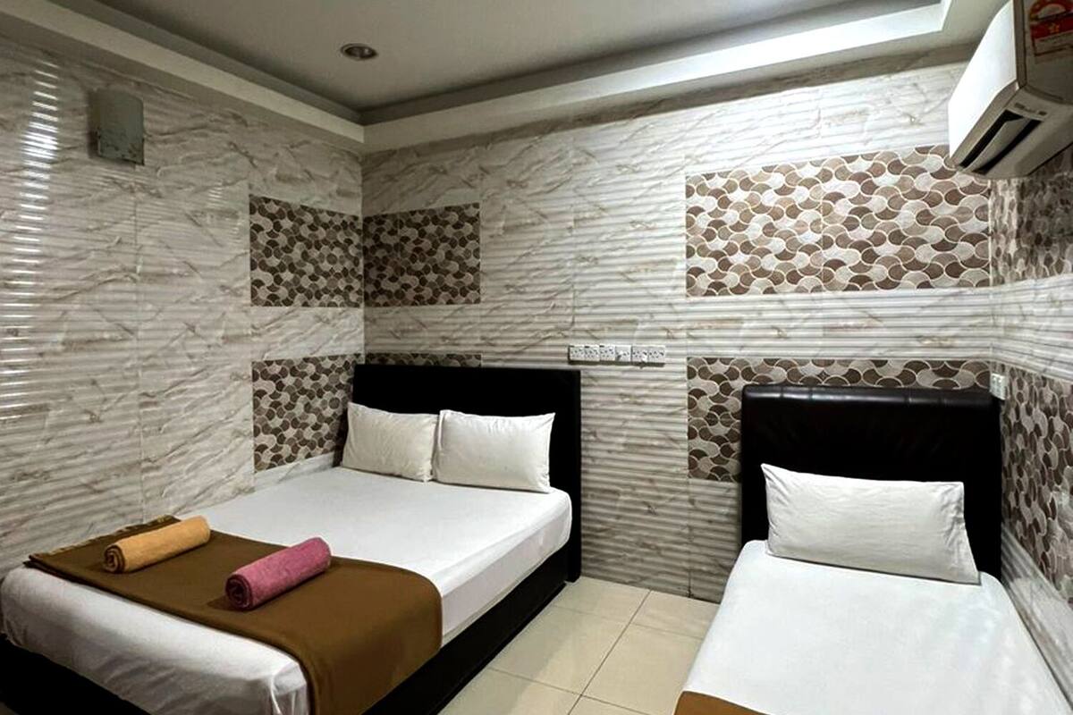 Ein Hotelzimmer mit zwei Betten, jeweils mit brauner Bettdecke und weißen Leinen. Die Wände sind mit einem gemusterten Fliesendesign versehen, und es gibt eine Deckenleuchte.