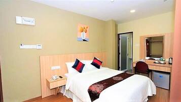 A hotel room with a bed, bedside table, phone, and a desk with a chair.