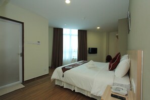 Una habitación de hotel con cama, mesita de noche con teléfono, televisor en la pared y puerta.