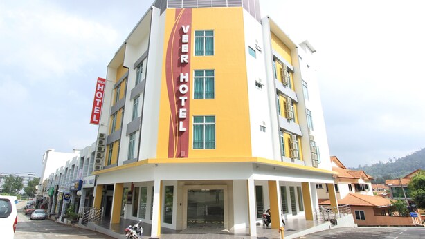 Et hotel med en gul og hvid facade, et tydeligt 'VEER HOTEL' skilt, og et overdækket indgangsparti.