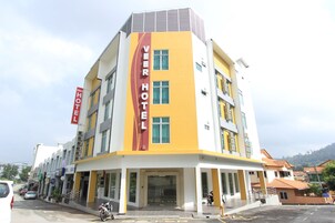 Un hotel con fachada amarilla y blanca, un llamativo letrero que dice 'VEER HOTEL' y un área de entrada cubierta.
