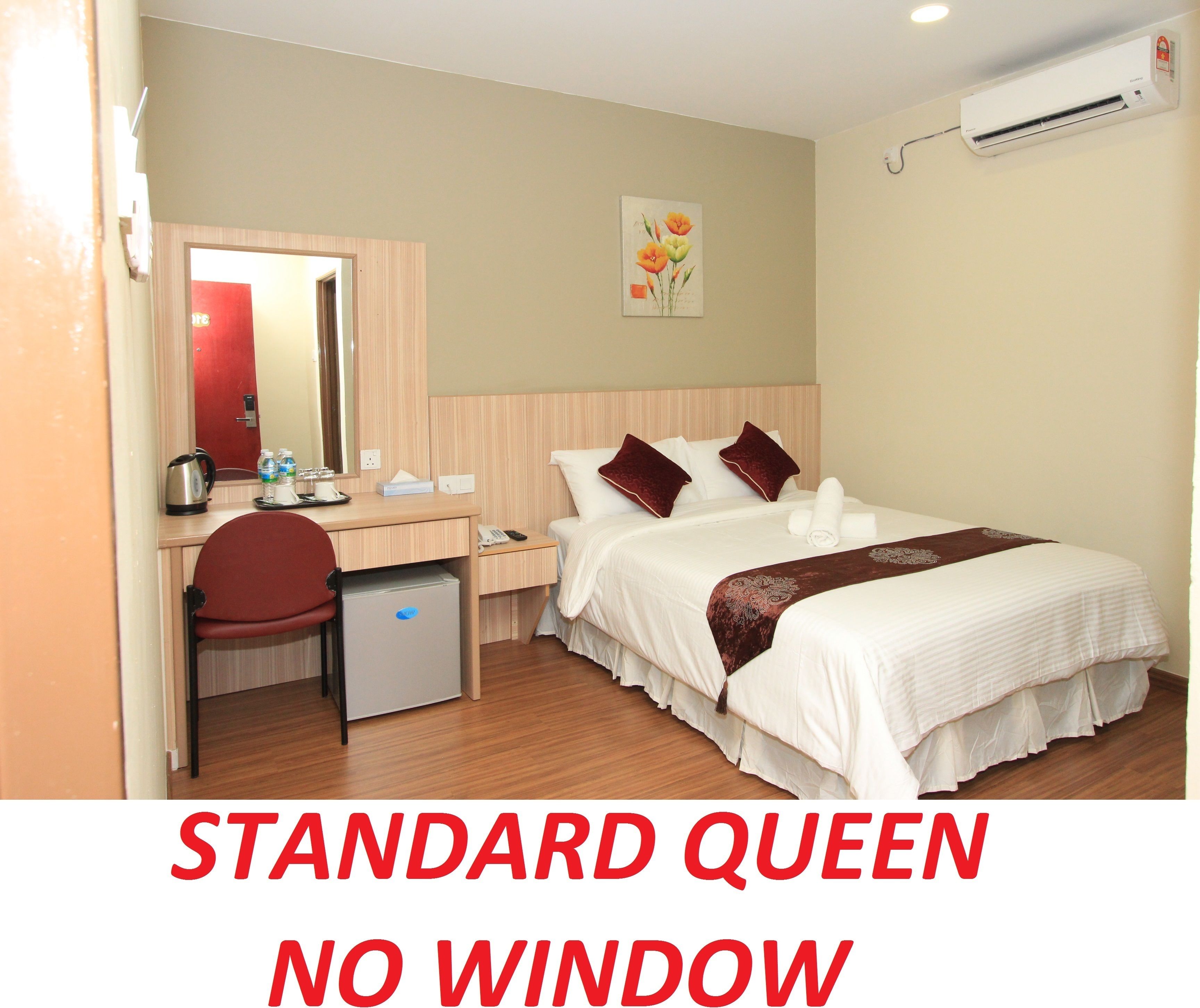 A standard queen bed with no window, a desk with a chair, a small refrigerator, and a mirror.