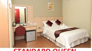 A standard queen bed with no window, a desk with a chair, a small refrigerator, and a mirror.