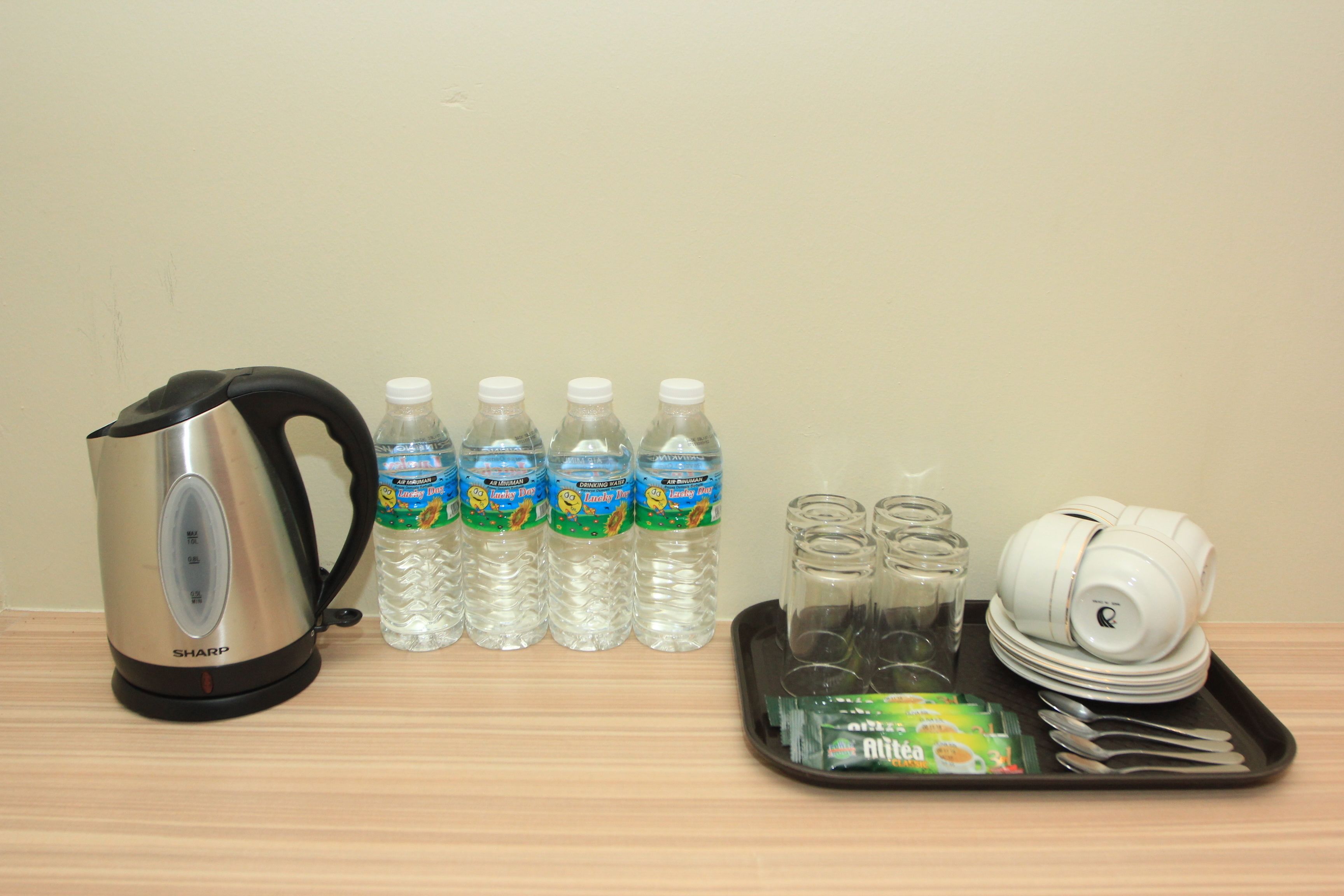 A kitchen setup with a kettle, water bottles, glass jars, a tray with utensils, and a stack of plates.