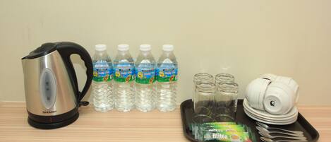 A kitchen setup with a kettle, water bottles, glass jars, a tray with utensils, and a stack of plates.